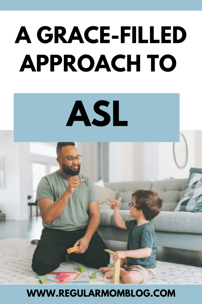 A black man sits on the living room floor with his white son who is wearing glasses. They are playing with toys and signing in ASL.