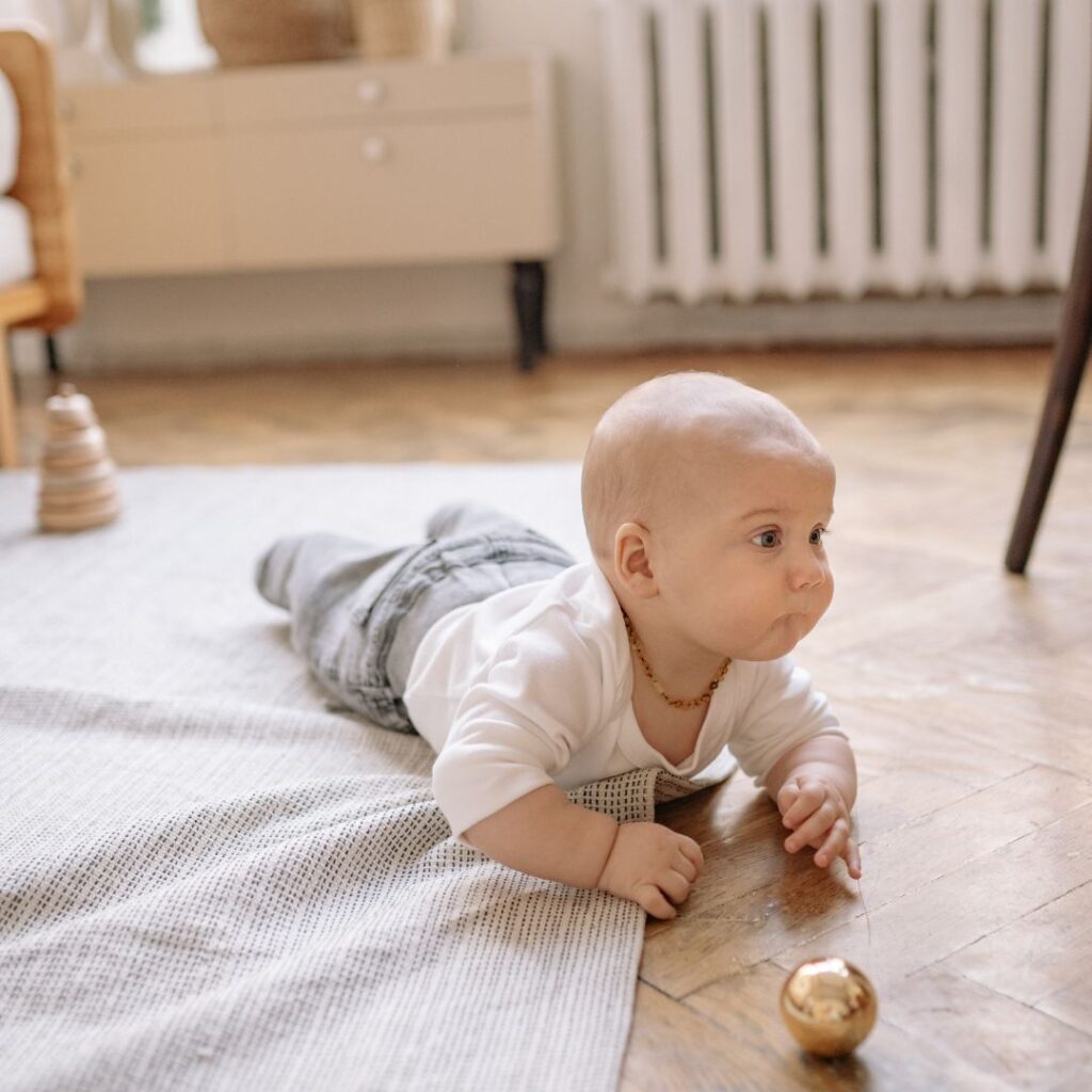 A baby boy is crawling on a blanket toward a gold ball on the floor to play a peek a boo sensory activity for babies.