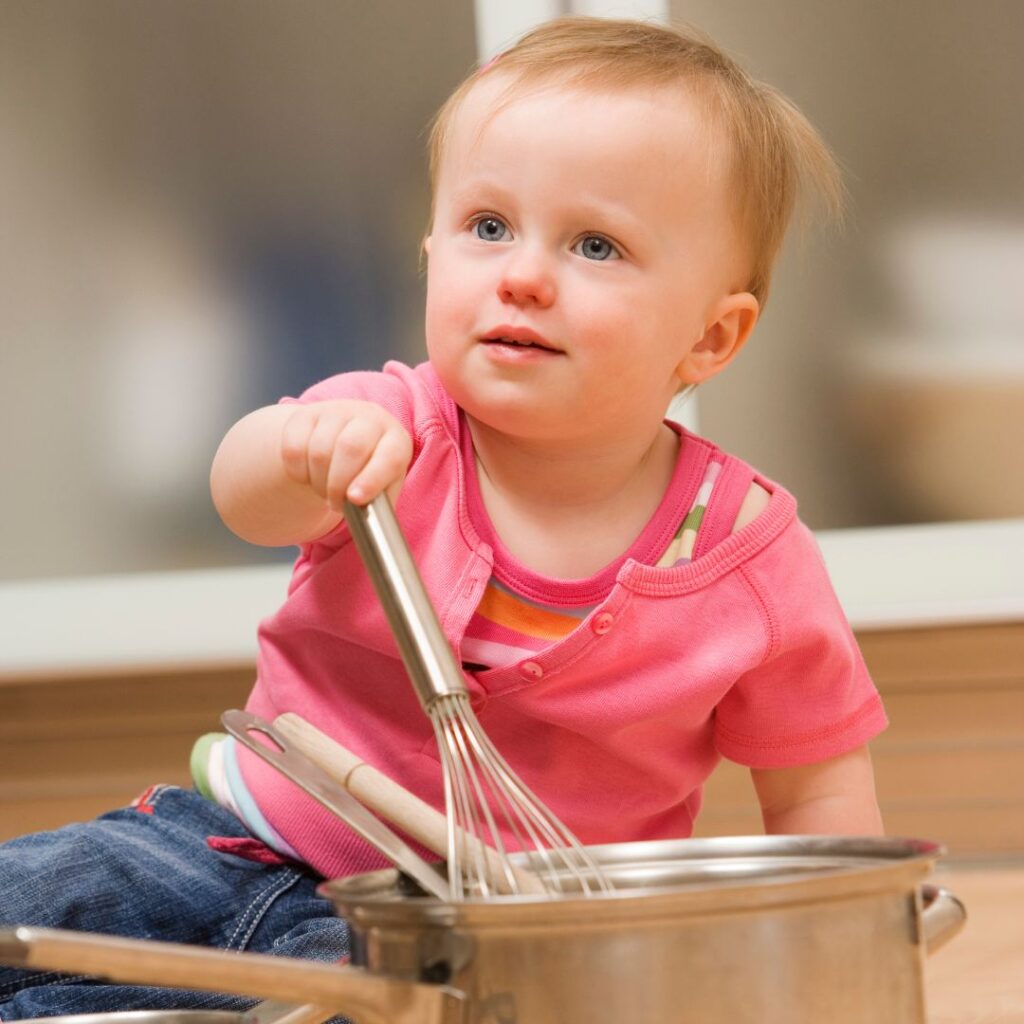 baby on the floor playing with a whisk and pots from the kitchen for sensory music activities for babies