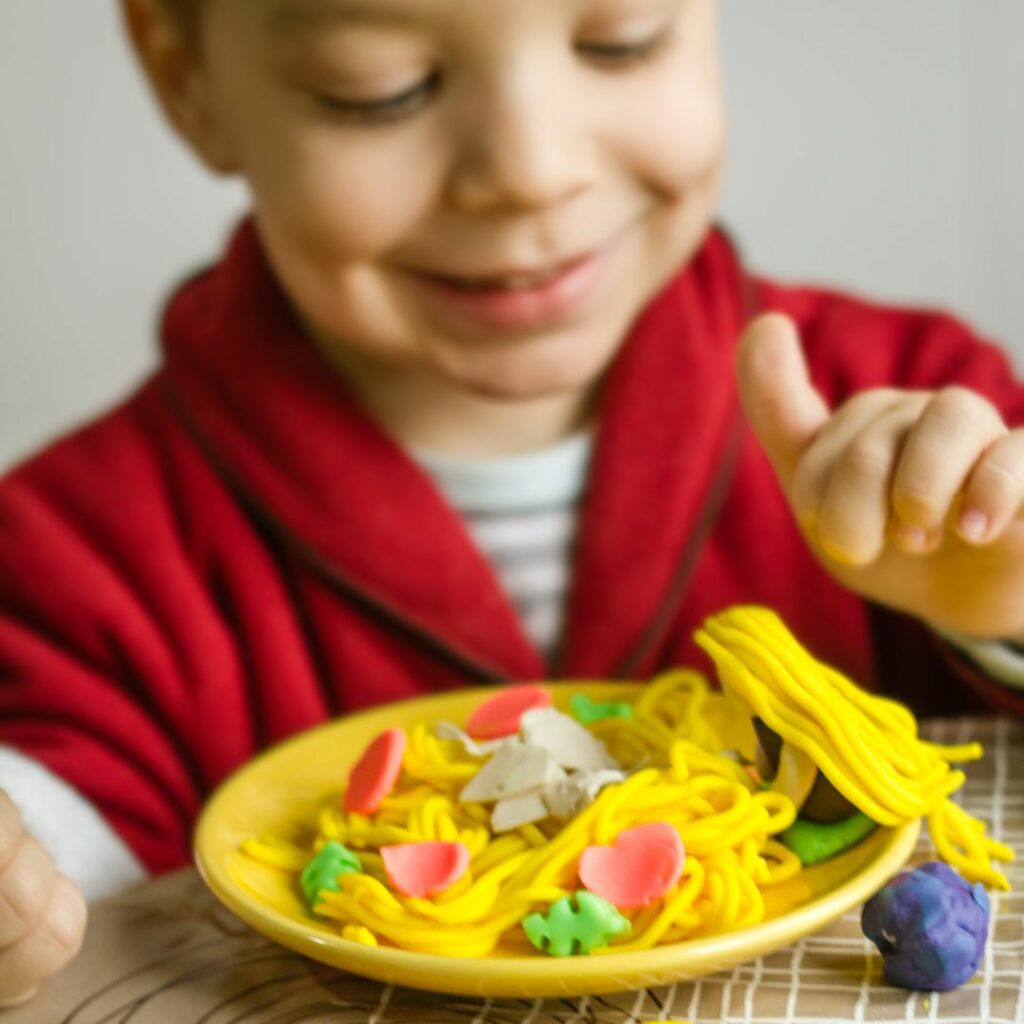A boy creates a playdough creation of pretend spaghetti.