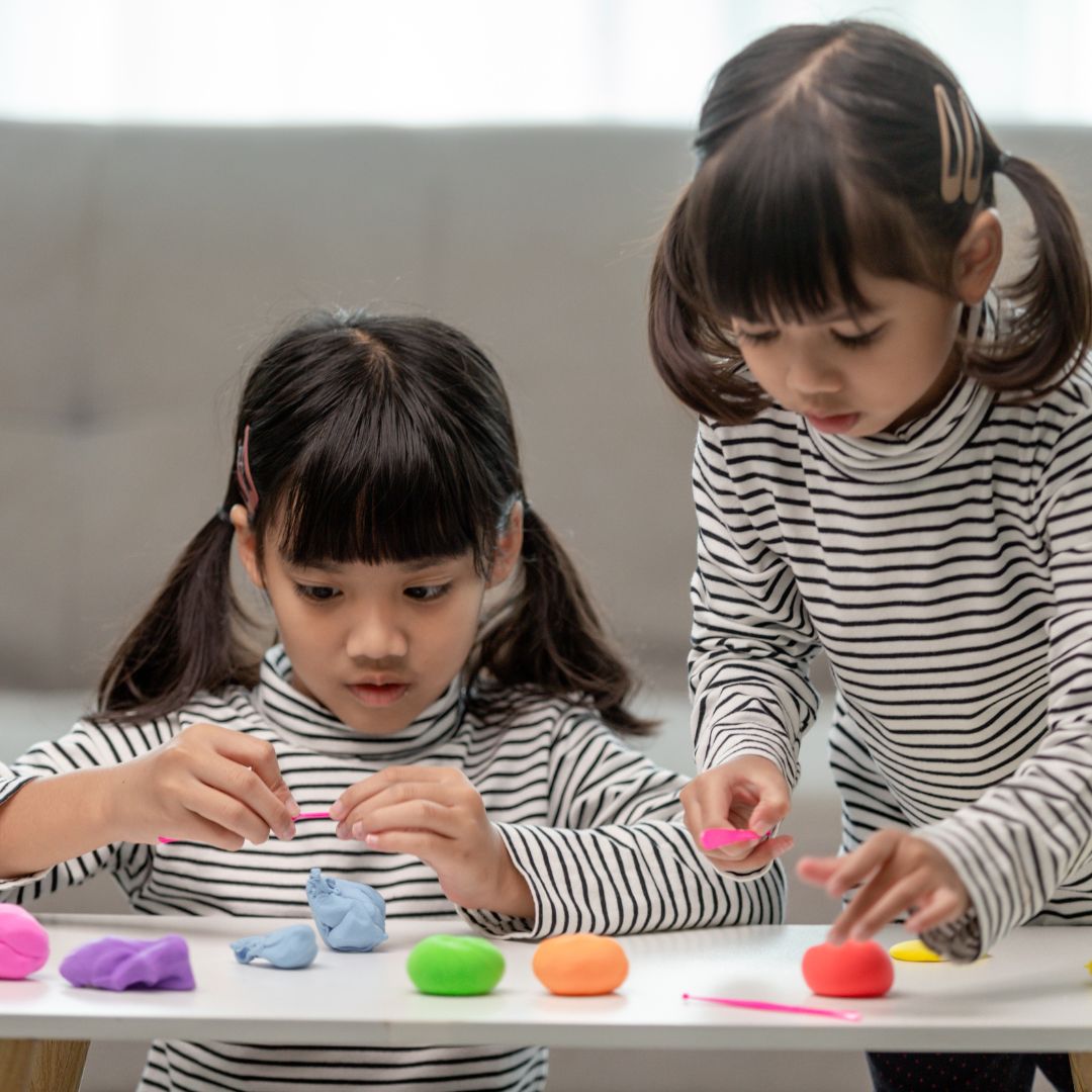 two girls playing with playdough activities at a living room table