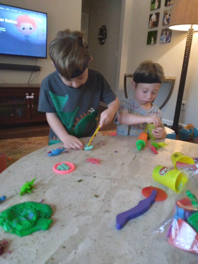 two boys with cochlear implants play with playdough activities on a living room table