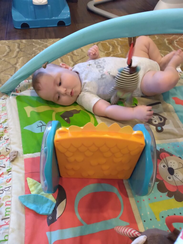 a baby laying on a play mat and looking at a mirror