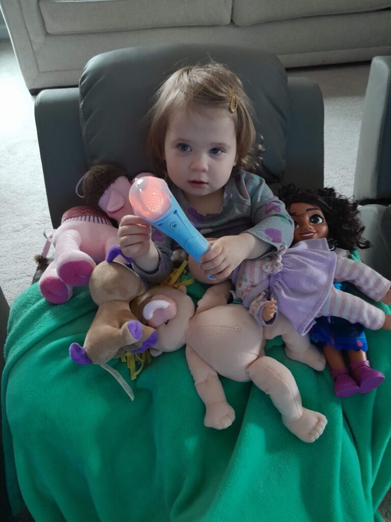 girl sitting in a chair surrounded by stuffed animals holding a light up microphone.