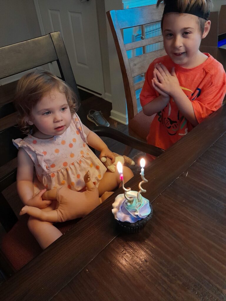 a baby girl and her brother sitting at a table with a cupcake with candles in front of them.