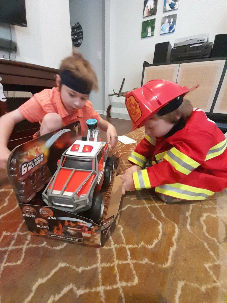 two boys in a living room playing with a jumbo fire truck
