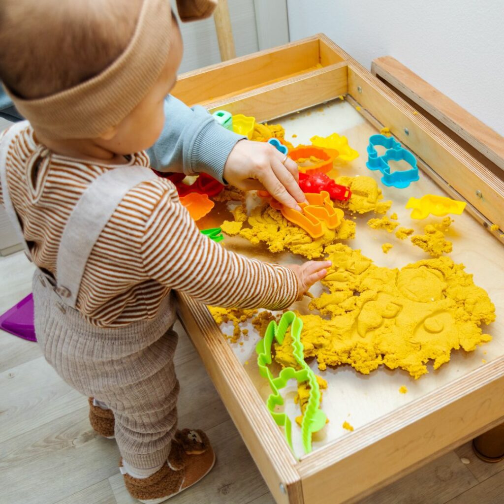 a toddler stands at a sensory table and plays sensory games with kinetci sand