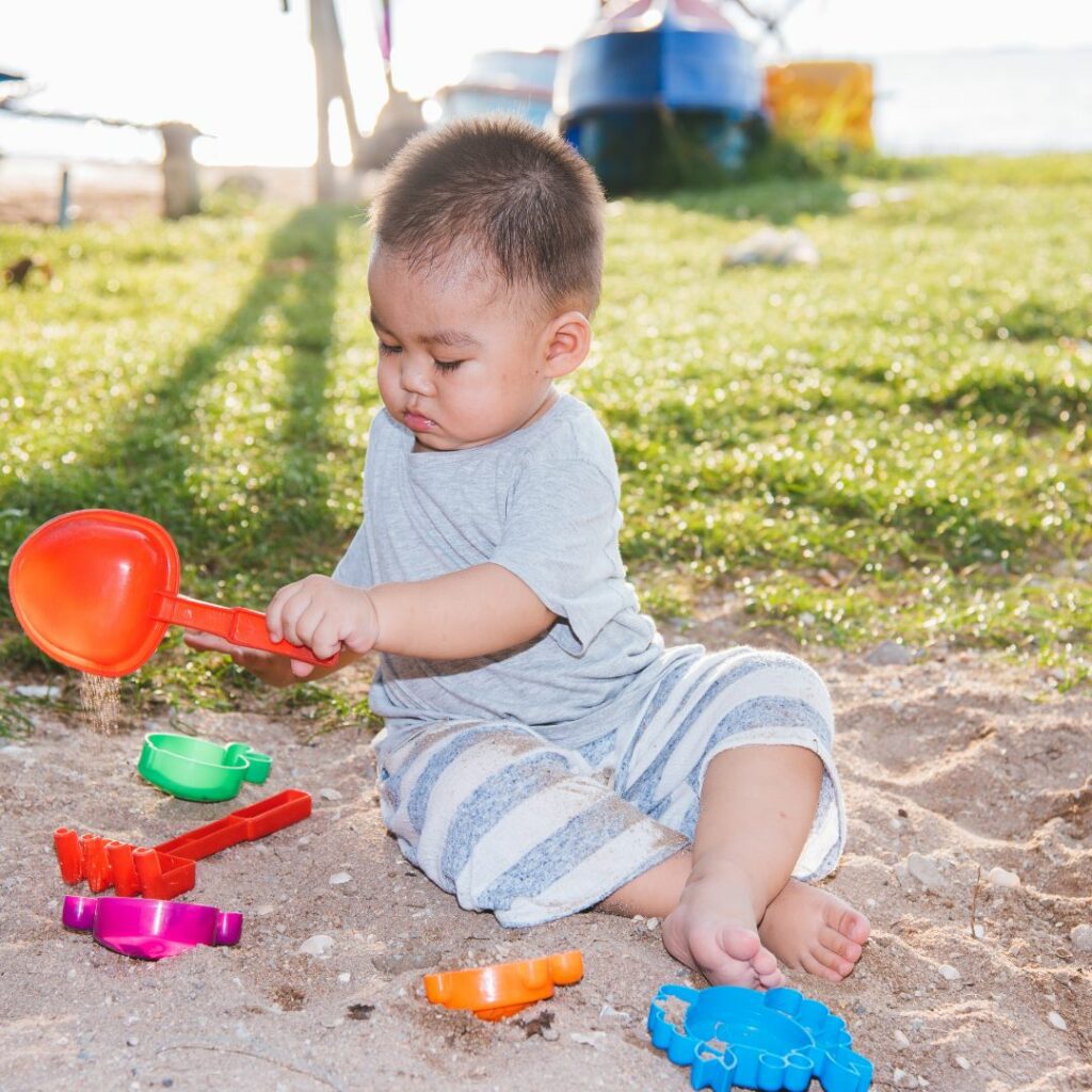 a baby sits in a sandbox and shovels and scoops sand