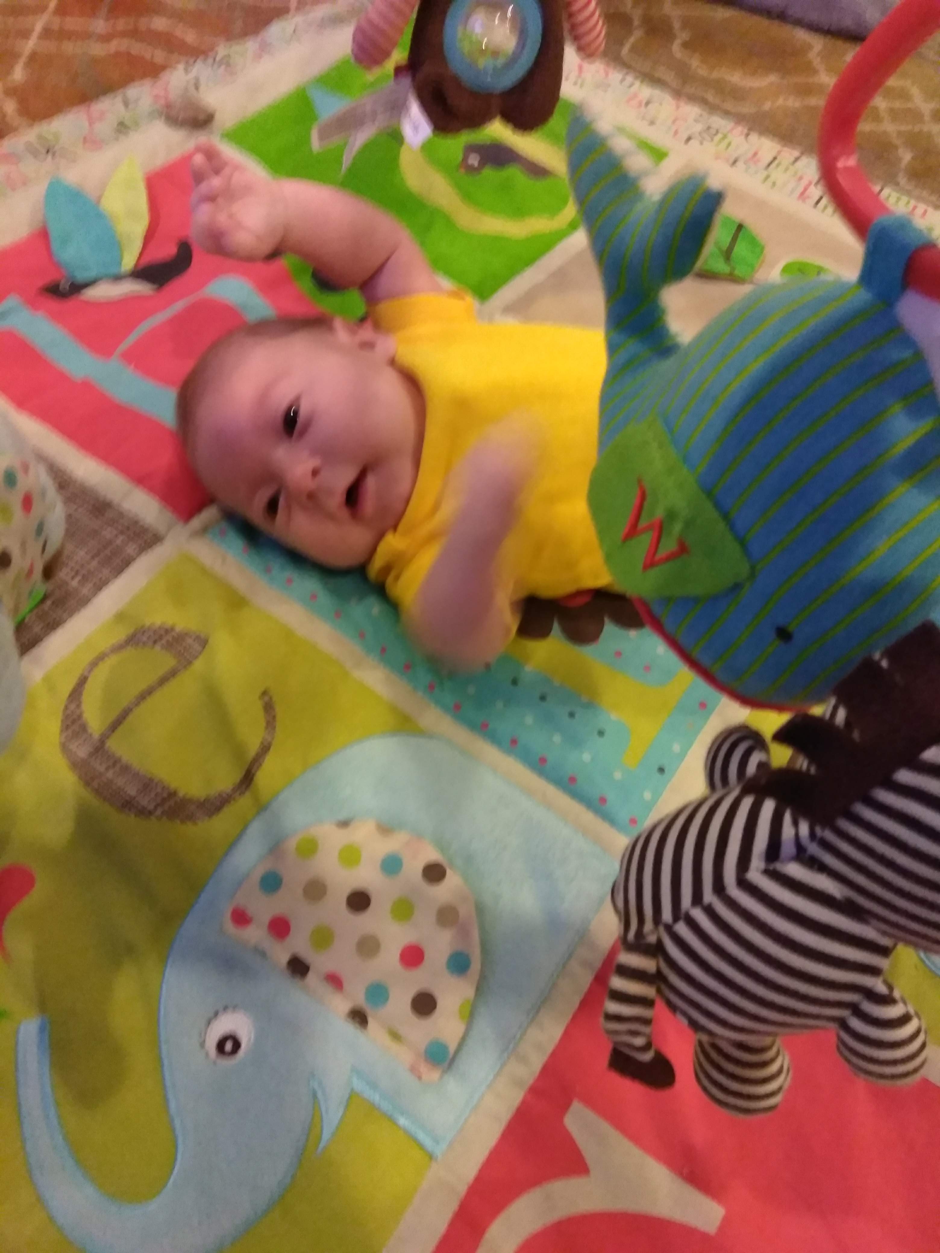 newborn baby laying on a play mat and looking at the items 