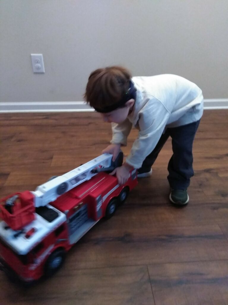 a boy standing in a hallway and playing with a large fire truck for a car and truck activity