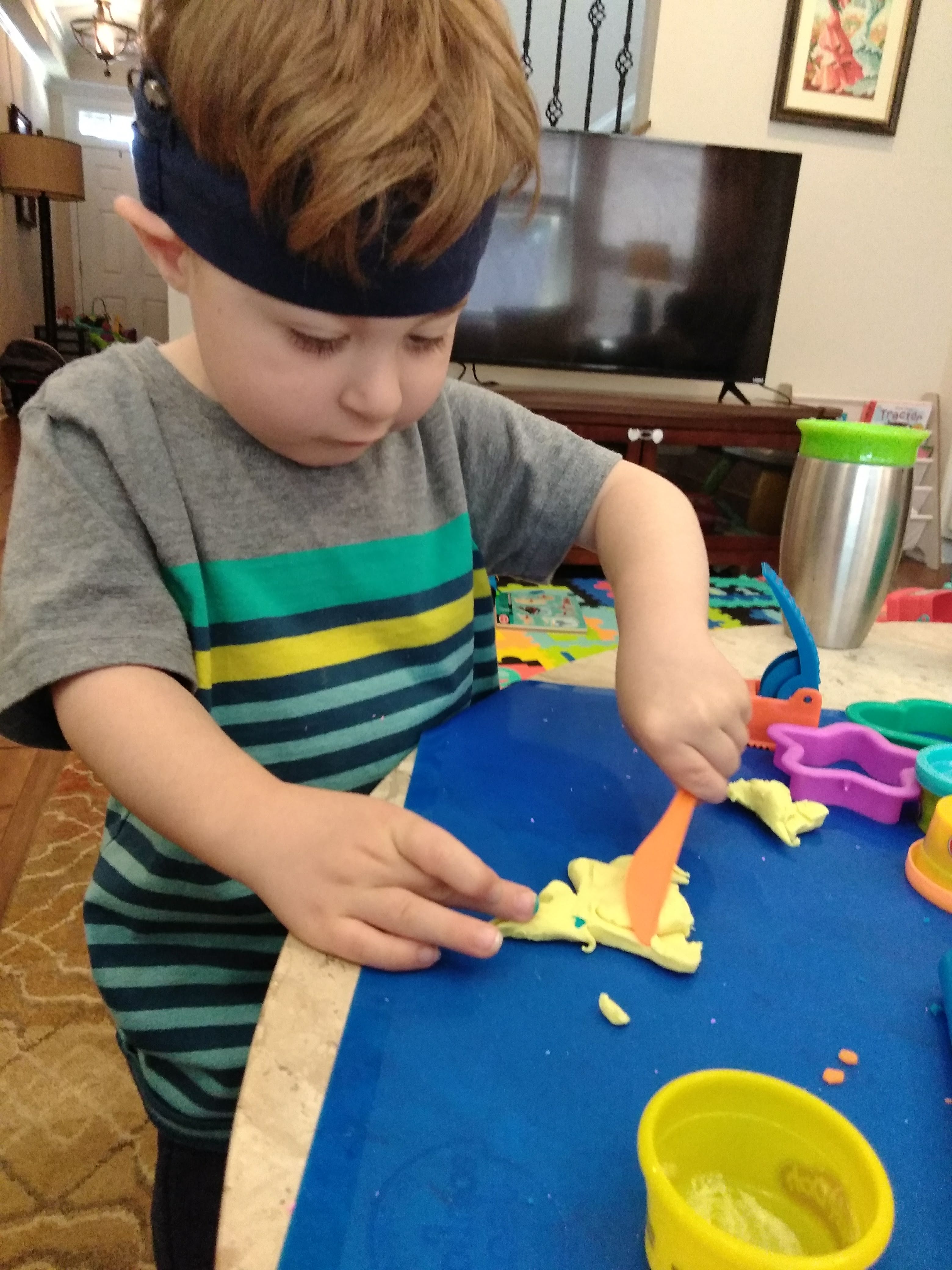 a boy with cochlear implants stands at a table and does playdough activities