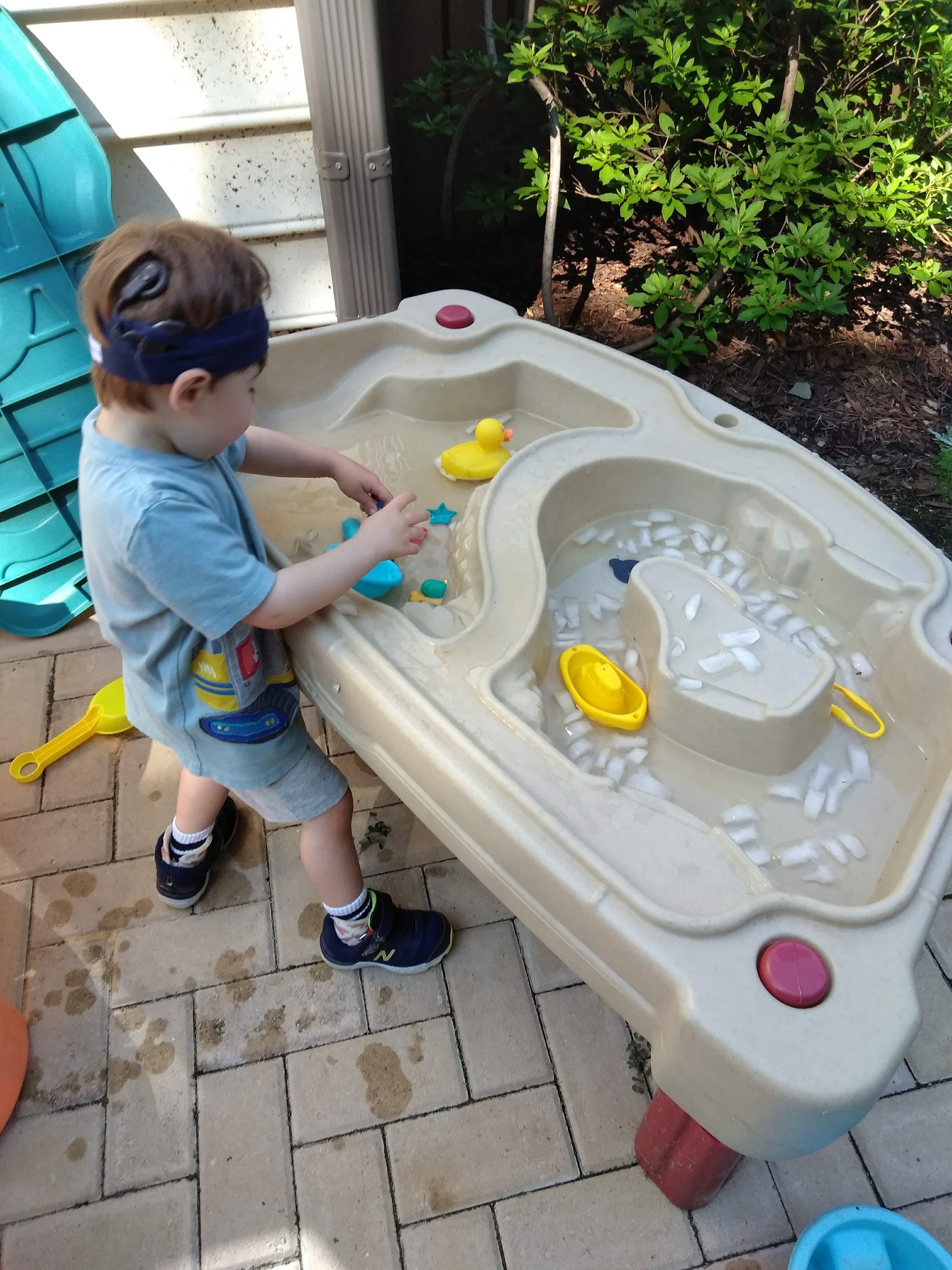 a boy standing at a water table with ice in it playing a water activity