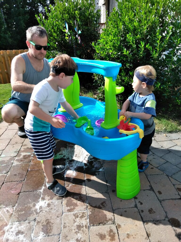 two boys standing outside in the summer at a water play table playing water activities for kids