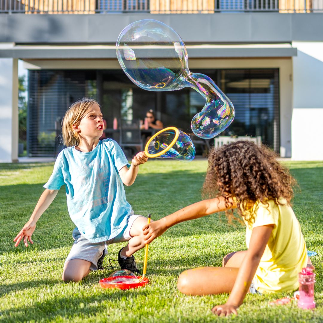 two kids sit on the lawn and blow and create bubbles