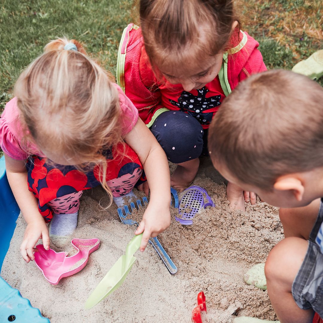 three kids playing sand activities in a small sandbox