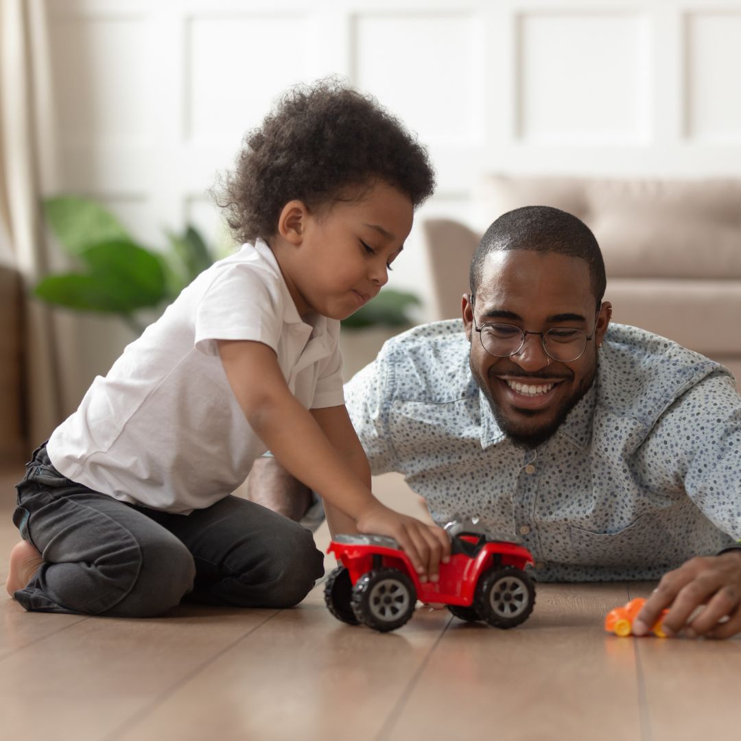 a black boy and his father play with a truck on the living room floor