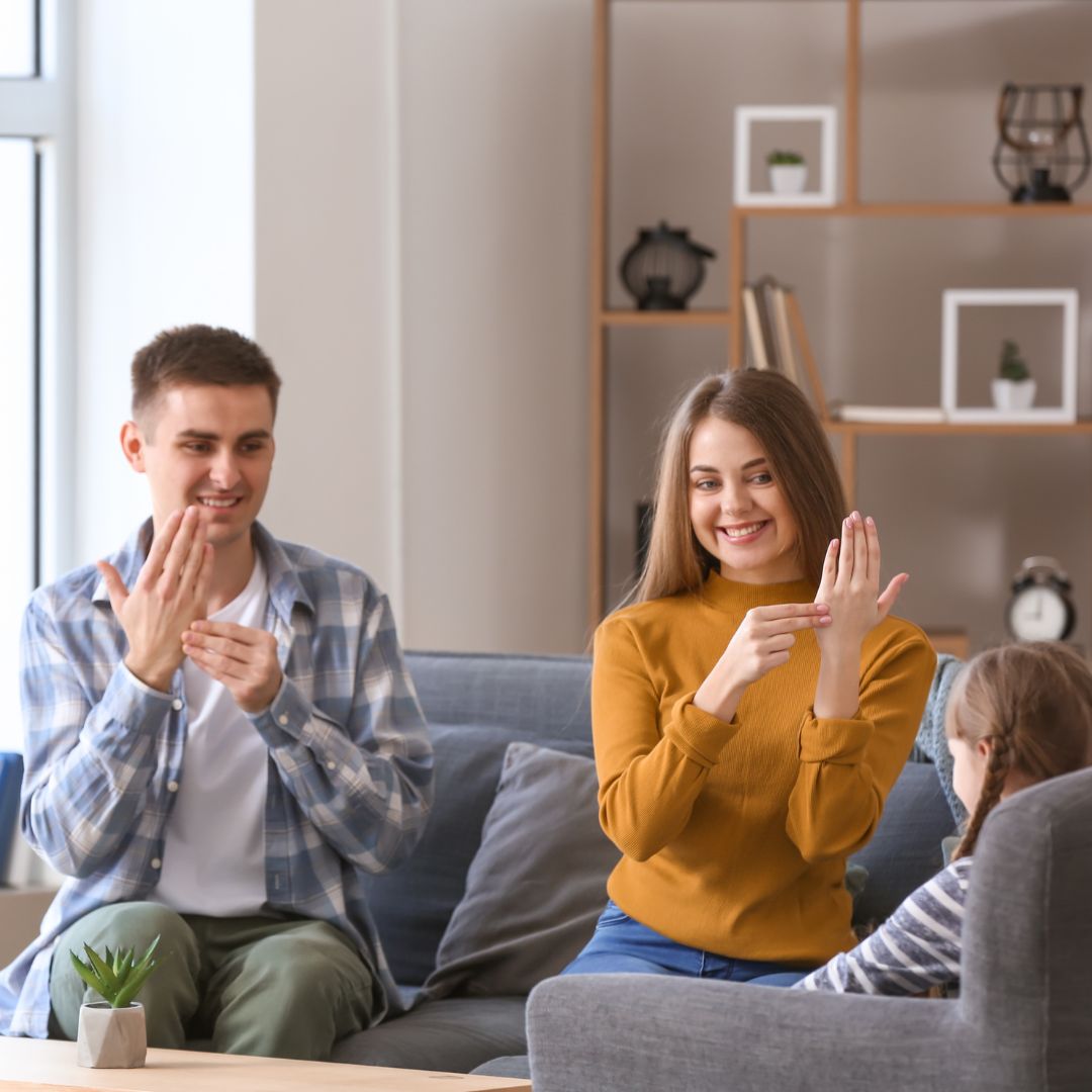 a man and woman sit on the couch in their living room and teach their daughter ASL