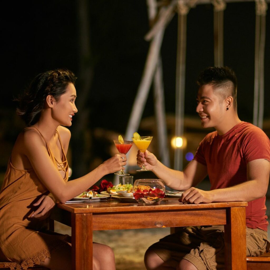 a asian man and woman cheers cocktails at a table on their outdoor patio for at home date nights for parents