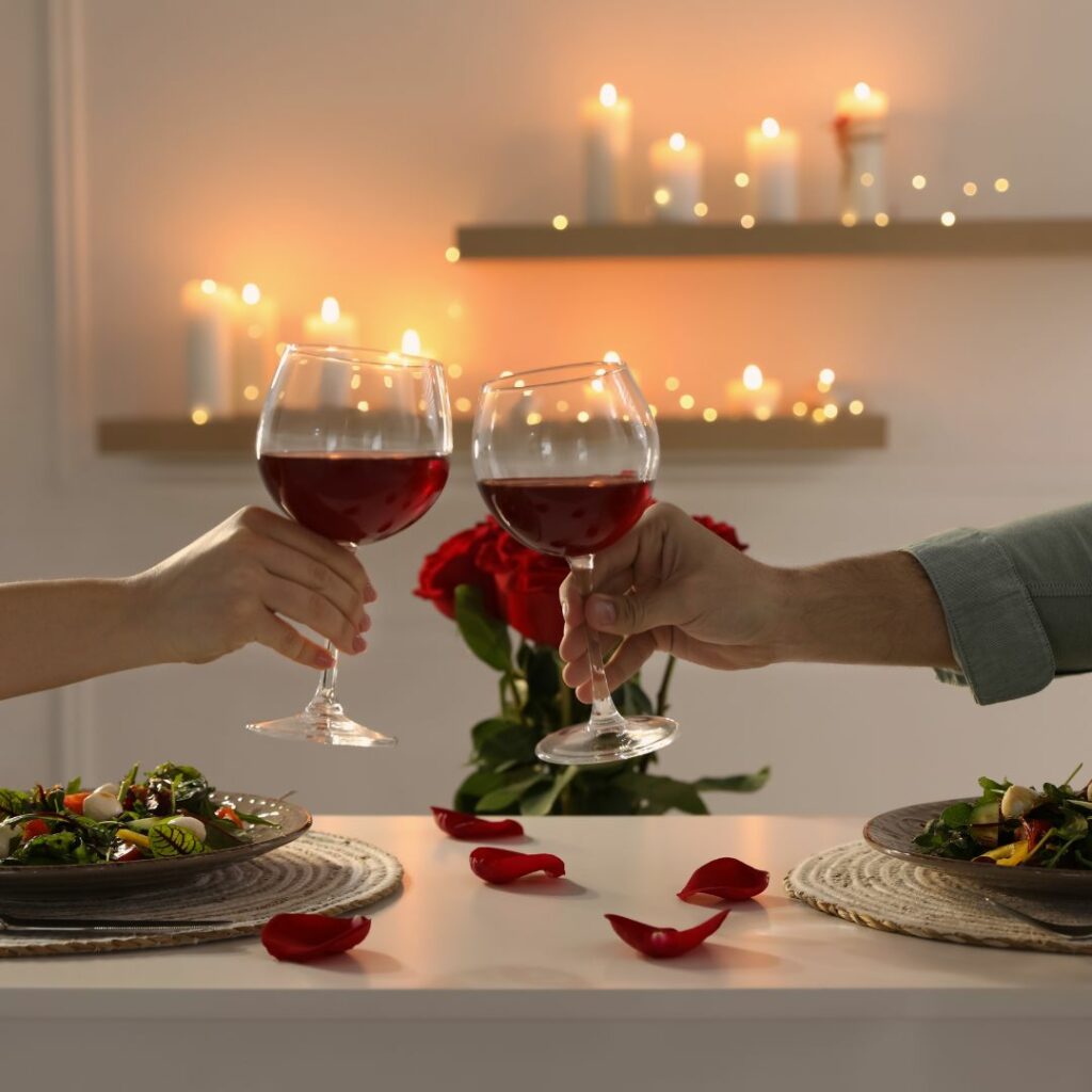 a table is set for a romantic dinner date and a couple cheers with glasses of wine over the table