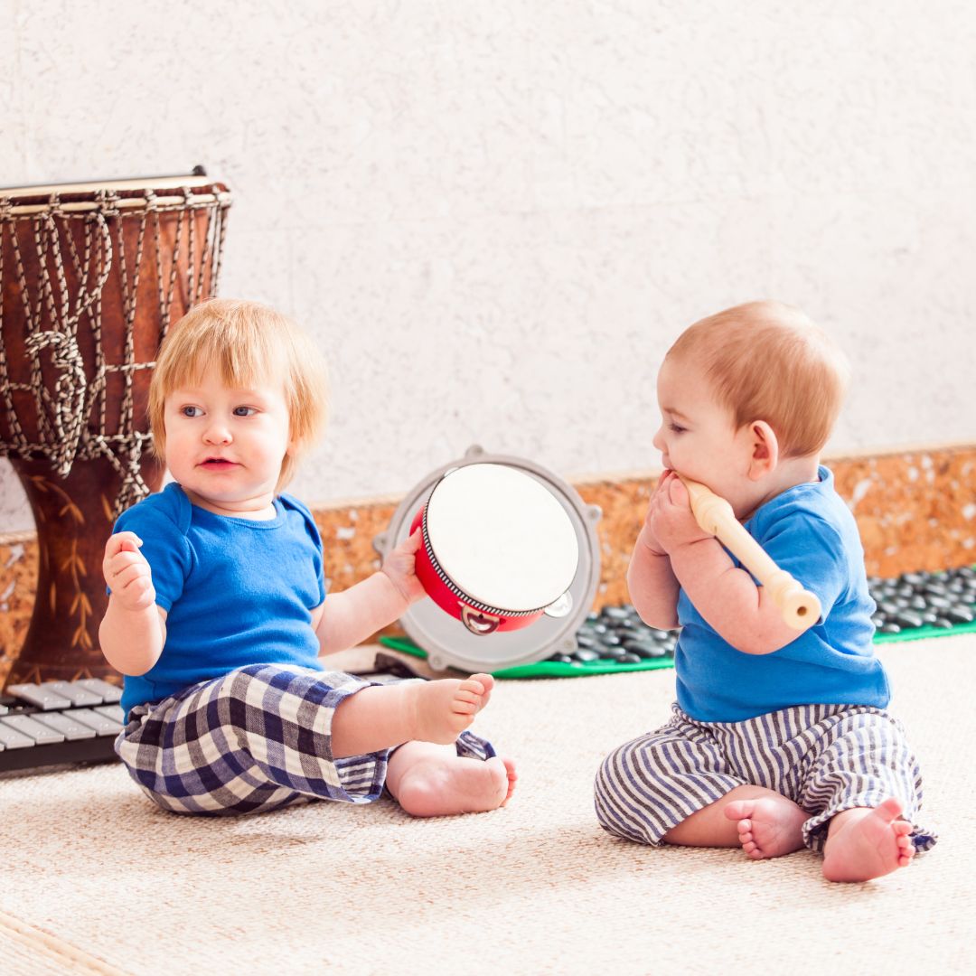 two babies sit on the floor and play musical instruments for hearing sensory activities