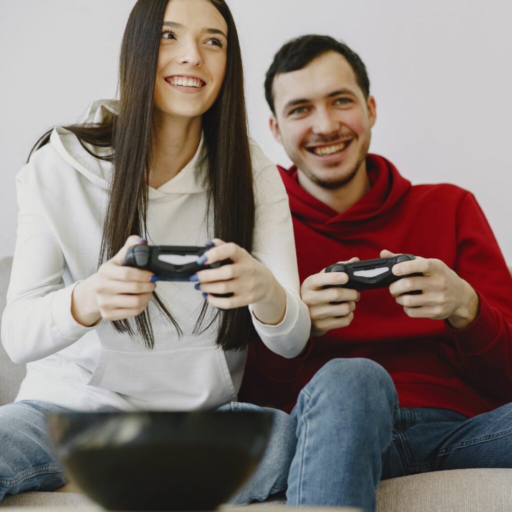 a woman and man sit on the couch and hold video game controllers to play games for at home game night for parents
