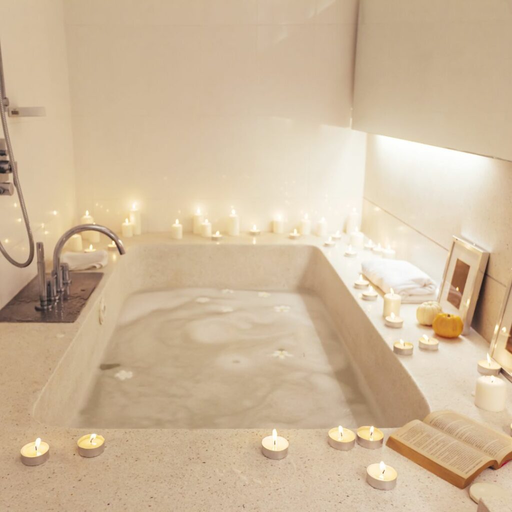 a big bathtub with candles lit around the edge and bubbles in the bath ready for an at home spa date night

