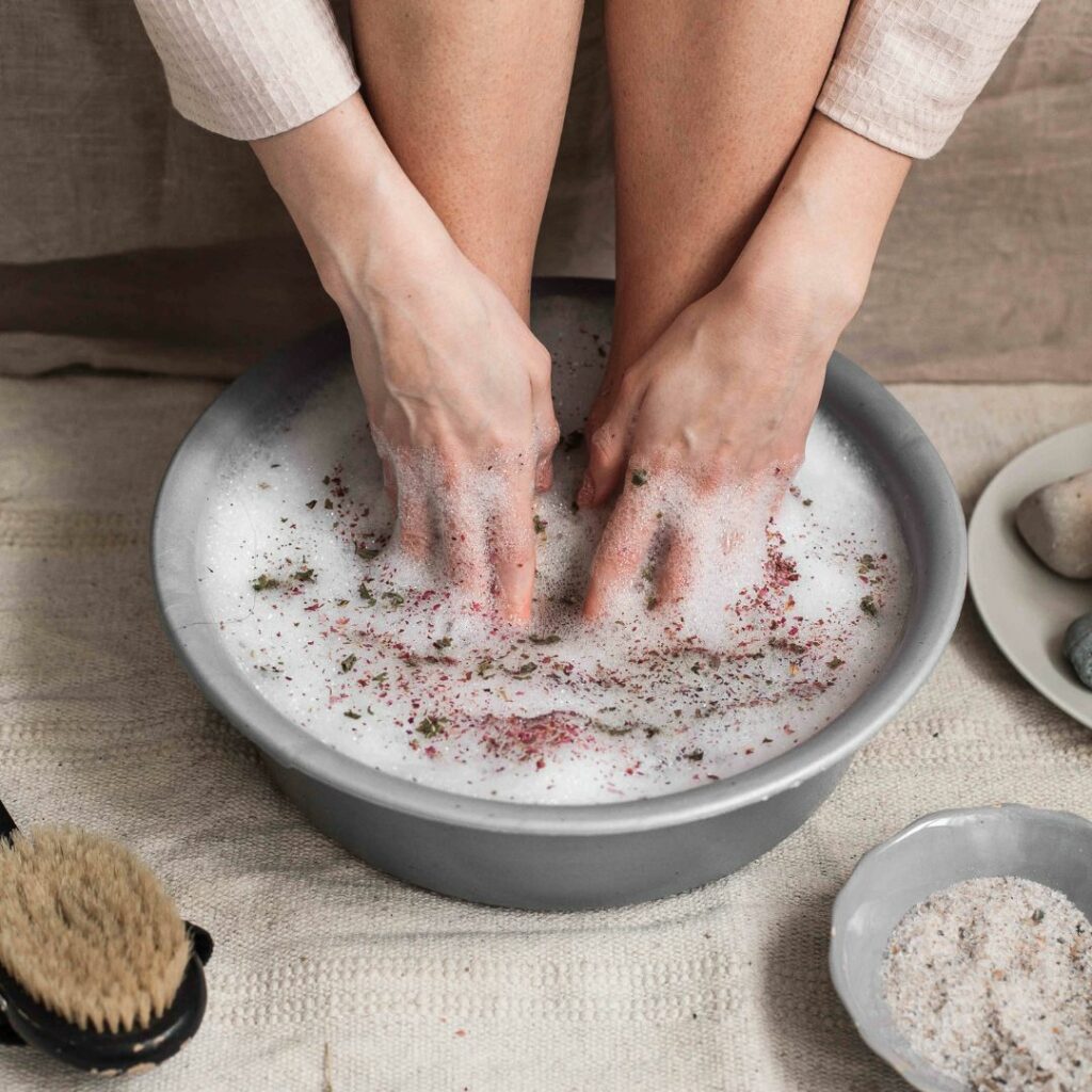 a woman sits with her feet in a bucket of soaking salts for an at home spa night