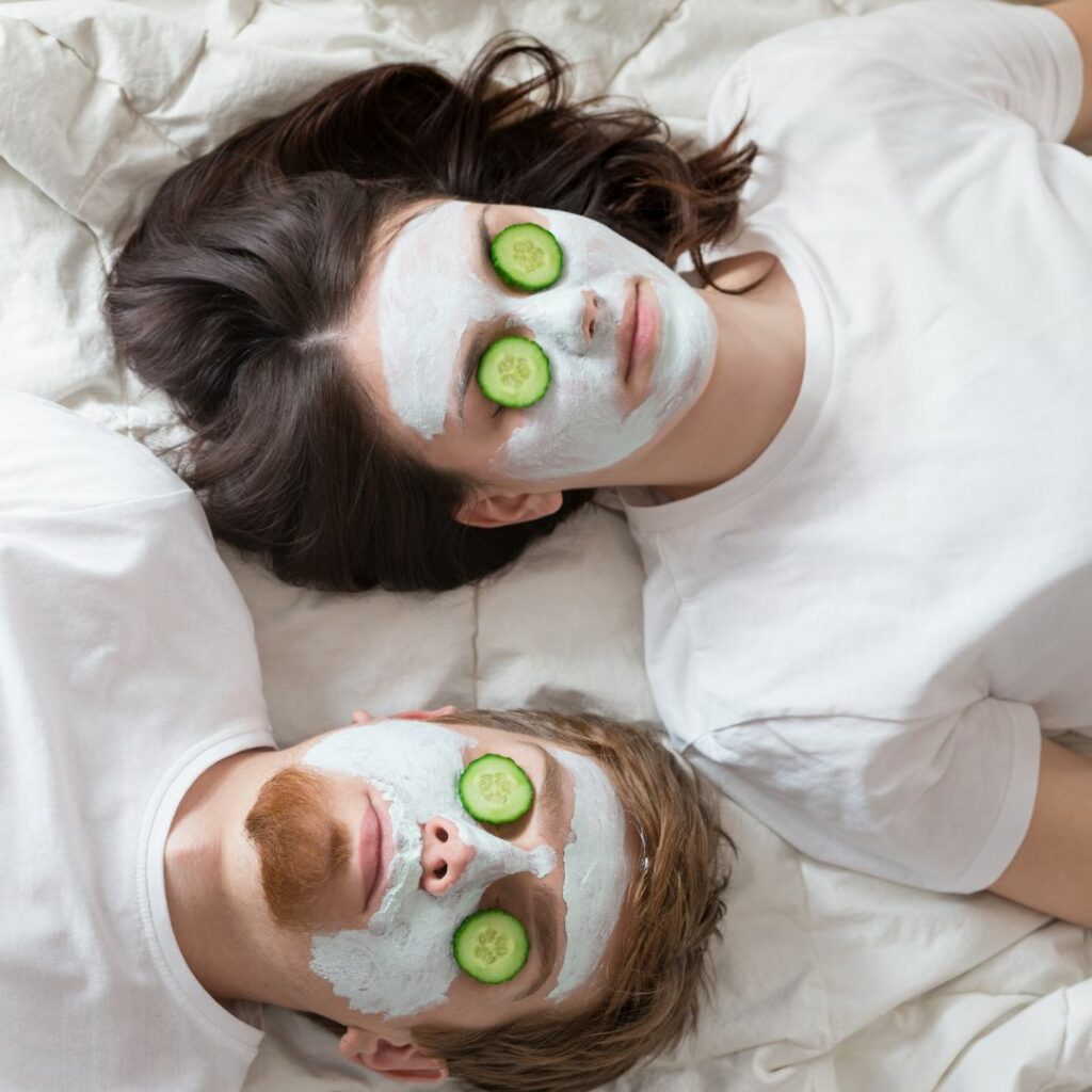 a man and woman lay on a bed and have yogurt masks on their face and cucumbers over their eyes for an at home spa night