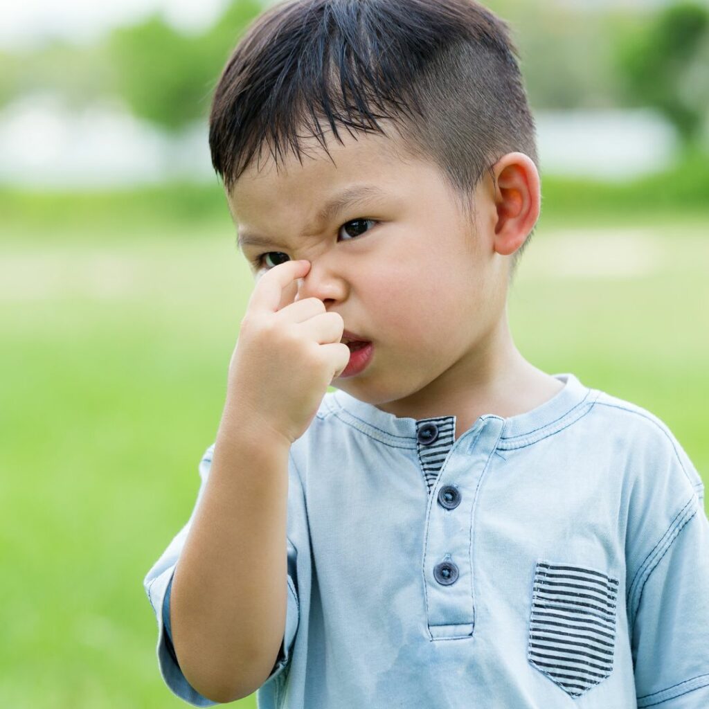 a toddler boy stands outside and scrunches up his nose for a sensory activity