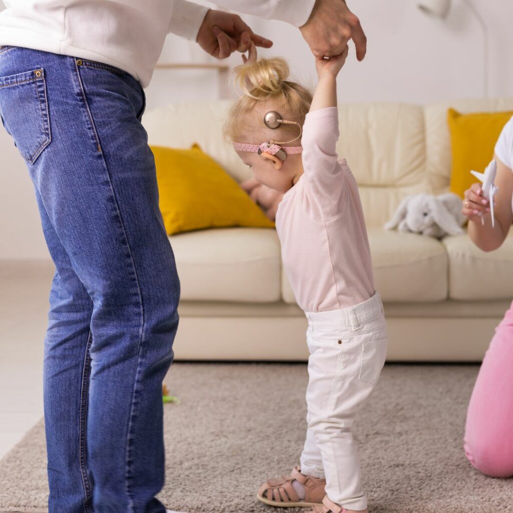 a toddler with cochlear implants dances in the living room with her father