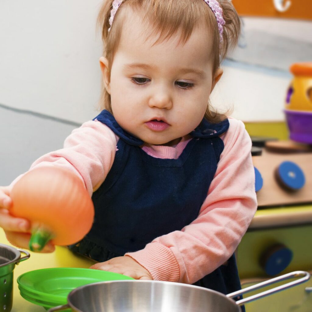 a baby girl plays with a pretend kitchen