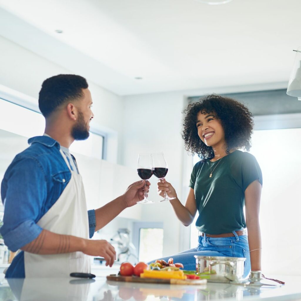 a couple stands in the kitchen and do cheers with wine glasses