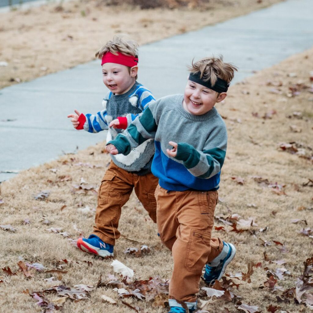 two little boys run around the yard outside and they are wearing headbands because they are kids with cochlear implants