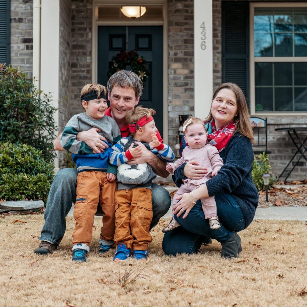 a family sit in front of their house for a picture. they have three children and two of their children are kids with cochlear implants