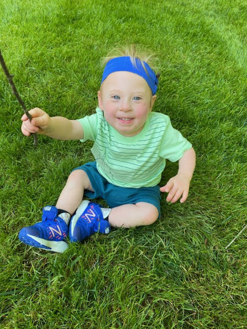 a 12 month baby sits on the grass and plays with a stick