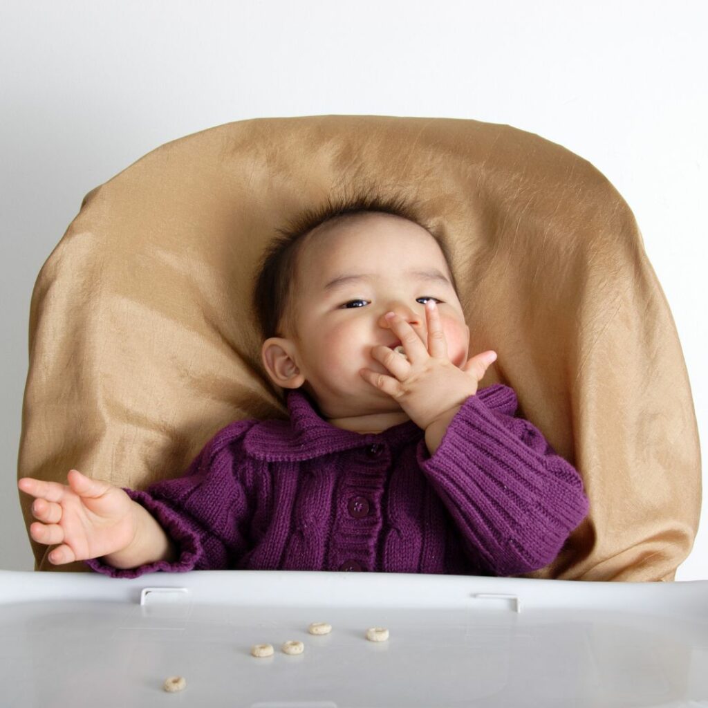 a baby sits in a high chair and eats cereal for a high chair sensory play activity