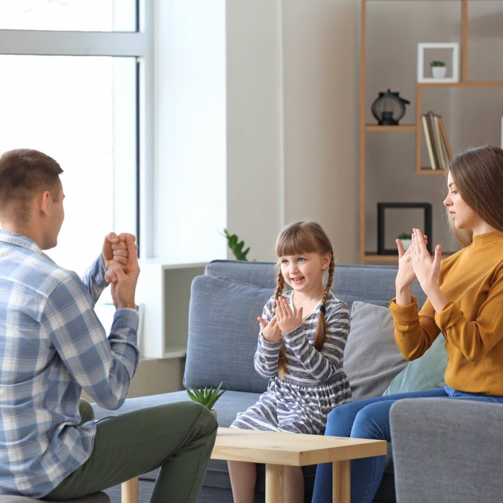 two parents and a child sit on the sofa in their living room and practice sign language together