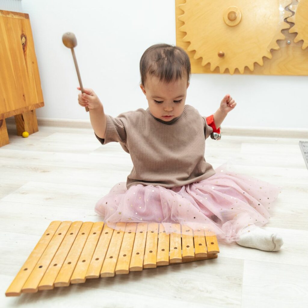a toddler sits on the floor and plays a big, wooden xylophone for sensory music activities for toddlers