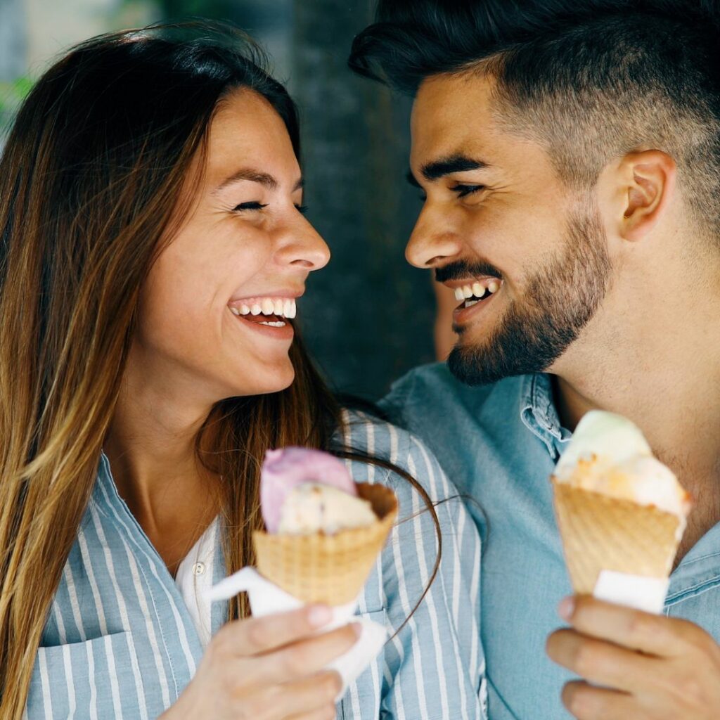 a man and a woman hold ice cream cones in their hands and stare and each other and laugh on a date night idea for parents