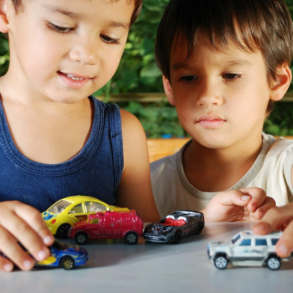 two boys stand at a table and play car sensory activities